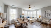 This well-appointed single-floor residence offers a thoughtfully designed open-concept layout that seamlessly connects the living, dining, and kitchen areas. The living room is bathed in natural light from a wraparound arrangement of large windows dressed with sheer white curtains and wood blinds, creating an airy, inviting atmosphere. Wood-style flooring flows throughout the main living areas, adding warmth and continuity to the space.

The kitchen is a functional centerpiece, featuring white shaker-style cabinetry, a subway tile backsplash, stainless steel appliances, and a generous granite-topped island with an undermount sink. Pendant lighting overhead and additional natural light from a nearby window make this an ideal space for cooking and entertaining. The adjacent dining area accommodates a full-sized wooden table and opens directly to the living space, encouraging easy flow between rooms.

The bedroom is a serene retreat, carpeted for comfort and filled with soft natural light from wide windows. Two well-designed bathrooms serve the unit — one featuring a tub-shower combination with granite vanity countertops, and the other offering a walk-in glass shower alongside a soaking tub. Both bathrooms continue the clean, modern aesthetic with white cabinetry and wood-style flooring. A dedicated laundry area with a full-size washer rounds out this cohesive and functional floor plan.