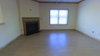 This two-floor home offers a thoughtfully designed layout that balances comfort and functionality across its multiple levels. The main living area immediately draws attention with its clean, open feel, highlighted by smooth hardwood flooring that extends throughout the space. A standout feature of the living room is the traditional fireplace, framed by a handsome wood mantel with a dark surround, providing a welcoming focal point for the room. A large window adjacent to the fireplace allows ample natural light to flood the interior, offering views of the surrounding outdoor scenery and creating a bright, airy atmosphere. Neutral-toned walls, complemented by warm wood baseboards and crown molding details, lend the space a cohesive and classic aesthetic. A ceiling fan fitting is present overhead, adding to the practical appeal of the living area. The two-floor configuration provides a clear separation of living and private spaces, with the upper level offering additional rooms suited for bedrooms or flexible use. Throughout the home, the consistent use of warm wood tones and light wall colors creates a unified and inviting ambiance, making this a well-rounded and move-in-ready property suitable for a variety of lifestyles.