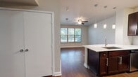 This efficiently designed one-bedroom, one-bathroom unit offers a thoughtful layout across a single floor, making excellent use of every square foot. The open-concept kitchen and living area forms the heart of the space, anchored by a striking peninsula with a white countertop, an integrated sink, and pendant lighting overhead. Rich dark wood cabinetry lines the kitchen walls, complemented by stainless steel appliances including a range, microwave, and refrigerator, as well as a classic subway tile backsplash. Dark hardwood-style flooring runs throughout the main living areas, adding warmth and continuity, while a ceiling fan and a large window allow natural light to fill the living room and provide outdoor views.

The bedroom is a comfortable, well-lit retreat featuring soft carpeting, a ceiling fan, and a window overlooking greenery outside. Two closets offer generous storage for the space. The full bathroom is neatly appointed with dark wood cabinetry, a white countertop vanity, a tiled soaking tub and shower combination, and matching hardwood-style flooring. Additional conveniences include a dedicated laundry area, a pantry, and a hallway connecting the rooms. Neutral gray walls throughout create a clean, cohesive aesthetic well-suited to a variety of décor styles.