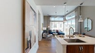 This thoughtfully designed single-floor residence combines contemporary style with functional living. The open-concept layout seamlessly connects the kitchen, dining, and living areas, creating a cohesive and airy atmosphere throughout. Warm hardwood flooring runs through the main living spaces, complemented by soaring ceilings and an abundance of natural light.

The kitchen is a standout feature, showcasing a two-tone design with crisp white upper cabinetry and rich walnut lower cabinetry, a large quartz waterfall island with seating, stainless steel appliances, a tile backsplash, and modern pendant lighting. The living room is anchored by expansive floor-to-ceiling windows that flood the space with sunlight and offer open views of the surrounding area.

The bedrooms provide a serene retreat, featuring plush carpeting, decorative accent wallpaper, and generous windows with sheer drapery. The primary bedroom connects to a well-appointed en-suite bathroom complete with a glass-enclosed walk-in shower, dark quartz countertops, white cabinetry, large-format tile flooring, and access to a spacious walk-in closet. A second bedroom offers its own bathroom access, also finished with stylish fixtures and warm tones. Throughout the residence, curated design details and a cohesive modern aesthetic create a welcoming and refined living environment.