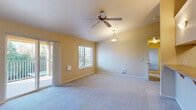 This single-floor residence offers a practical and comfortable layout across three bedrooms, one bathroom, and two connecting hallways. The living area is bright and generously proportioned, featuring warm yellow-toned walls, plush carpeting, and a ceiling fan with pendant lighting. Sliding glass doors open directly onto a private balcony, filling the room with natural light and outdoor views, while a secondary window further enhances the airy feel. The kitchen is designed with functionality in mind, featuring a pass-through breakfast bar that connects openly to the living area, warm-toned cabinetry, a stainless steel sink, tile countertops, and standard appliances including a range, microwave, and refrigerator. An in-unit washer and dryer are conveniently tucked just beyond the kitchen on wood-look flooring. The bedrooms are carpeted and well-lit, with the primary bedroom accommodating a comfortable footprint. Secondary bedrooms offer bright windows and built-in closets with shelving. The bathroom is cleanly appointed with a light wood vanity, tile countertop, a large mirror, and wood-look flooring. Warm neutral tones and consistent finishes throughout create a cohesive and livable atmosphere.