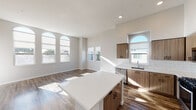 This thoughtfully designed single-floor residence combines modern aesthetics with functional living. The open-concept kitchen and living area serves as the heart of the home, featuring soaring ceilings that amplify the sense of space. The kitchen is equipped with stainless steel appliances—including a gas range, microwave, and refrigerator—complemented by warm wood-toned cabinetry, a white quartz island, subway tile backsplash, and a stainless steel sink. A series of striking arched windows floods the space with abundant natural light and offers views of the surrounding neighborhood, including glimpses of palm trees that hint at a Southern California setting. Rich wood-look flooring flows throughout the main living areas, adding warmth and continuity. The bedrooms are carpeted for comfort and feature ample natural light through large windows; the primary bedroom includes access to a walk-in closet. Two well-appointed bathrooms include combination tub-and-shower units, wood-toned vanities, white quartz countertops, and large mirrors. A private entry with covered porch and an exterior wall sconce adds curb appeal. The residence is finished with a neutral color palette, recessed lighting, and modern hardware throughout, creating a clean, contemporary ambiance.