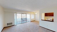 This single-floor residence offers a thoughtful, functional layout designed for comfortable everyday living. The spacious living room is a standout feature, finished with plush wall-to-wall carpeting and bathed in natural light streaming through large sliding glass doors that open onto a private balcony overlooking a wooded outdoor setting. A ceiling fan overhead adds both comfort and practicality. An accent brick wall adds a touch of character to the living area, while a pass-through window connects seamlessly to the kitchen, enhancing the open feel of the space. The kitchen is well-appointed with rich, dark wood cabinetry offering generous storage, laminate countertops, white appliances including a range and refrigerator, a dishwasher, and hardwood flooring that adds warmth underfoot. The two bedrooms are quiet and comfortable, each featuring soft carpeting, ceiling fans with integrated lighting, and windows dressed with blinds that allow for natural light. A dedicated closet provides convenient storage. The bathroom is clean and straightforward, featuring a full tub-shower combination, a toilet, vanity, and tile flooring. Textured ceilings and warm neutral tones throughout create a cohesive and inviting ambiance across the entire space.
