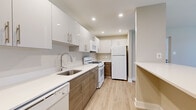 Located at 11 Thorn Ln in Newark, Delaware, this one-bedroom, one-bathroom residence offers a well-organized, single-floor layout designed for comfortable everyday living. The kitchen is a standout feature, showcasing contemporary wood-grain cabinetry with sleek bar-pull hardware, crisp white quartz countertops, a stainless steel sink with a modern gooseneck faucet, and a full suite of white appliances including a gas range, dishwasher, microwave, and refrigerator. Recessed lighting illuminates the space, and light wood-look flooring flows seamlessly throughout the kitchen and living areas, creating a cohesive, modern aesthetic. The open living room is bright and airy, featuring a sliding glass door with vertical blinds that invites natural light and provides outdoor access. Baseboard heating and wall-mounted AC units ensure year-round climate comfort. The bedroom is carpeted for warmth, with a window overlooking greenery, baseboard heating, and its own wall AC unit. The bathroom is finished in a clean, contemporary style with white cabinetry, quartz countertops, an undermount sink, and a large mirror. A convenient hallway connects all rooms, completing this efficiently designed and thoughtfully updated residence.