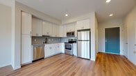 This single-floor unit showcases a thoughtfully designed open layout with consistent warm-toned hardwood flooring connecting the kitchen and living areas. The kitchen is well-appointed with white shaker-style cabinetry extending to the ceiling, providing ample storage. A grey subway tile backsplash adds texture, while stainless steel appliances — including a refrigerator, electric range, built-in microwave, and dishwasher — deliver a complete and functional cooking space. A matte black faucet at the undermount sink adds a modern contrast to the bright, neutral palette.

The open living area benefits from generous natural light, enhanced by a large sliding glass door that leads directly to a private balcony with outdoor views of surrounding greenery. Recessed lighting throughout the unit ensures consistent, clean illumination.

The bathroom maintains the same contemporary aesthetic, featuring large-format beige floor tiles, a white floating vanity with under-mount sink, and a full tub-shower combination with a crisp white surround. Recessed lighting and neutral wall tones keep the space feeling bright and functional. Overall, the unit presents a clean, modern ambiance suited for comfortable everyday living.