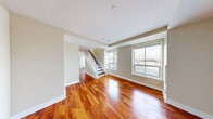 Located at 250 First Ave in Boston's Charlestown neighborhood, this two-bedroom, three-bathroom two-story residence offers a thoughtfully designed layout spread across two floors. The lower level features a spacious living area with gleaming rich-toned hardwood floors that extend throughout, a kitchen with dark stone countertops, light wood cabinetry, a center island, and stainless steel appliances. Large windows on the main floor invite abundant natural light and frame city views, while a classic white-railed staircase with dark wood treads connects the two levels. The upper floor houses the bedrooms, each carpeted for comfort. The generously sized primary bedroom features multiple windows with striking waterfront views and a built-in closet. The second bedroom also enjoys natural light and urban views. The three bathrooms offer a range of finishes, including a marble-tiled bathroom with a glass-enclosed shower and polished chrome fixtures, and a full bath with a tub-shower combination and crisp white subway tile. Neutral warm tones throughout create a clean, cohesive aesthetic, making this multi-floor residence a well-appointed and versatile home in Boston.
