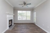 This single-floor residential space offers a well-organized layout designed for comfortable everyday living. The kitchen is a standout feature, equipped with light maple cabinetry, stone-toned laminate countertops, a stainless steel range with overhead ventilation, a stainless steel refrigerator, a built-in dishwasher, and a double-basin sink with a brass-finish faucet. Crown molding accents the kitchen ceiling, adding a refined touch. A peninsula counter extends into the adjoining area, creating a natural transition to the open living space, which features wood-look flooring throughout.

The bedroom is generously proportioned, finished with plush carpeting and neutral taupe walls. It includes direct access to a walk-in closet with built-in shelving, as well as a private exterior door that brings in natural light through a sidelight window. The full bathroom is clean and functional, featuring a single-basin vanity with a large mirror, a toilet, and a shower-tub combo enclosed by a door. Taupe wall tones carry throughout, lending a cohesive and understated aesthetic to the entire space. Together, the rooms create a practical and comfortable single-floor living environment.