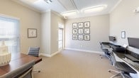 This single-floor professional office suite is designed to accommodate a variety of business functions within a polished, cohesive environment. The space is finished throughout with neutral warm-gray walls, white crown molding, and textured beige carpeting, creating a calm and professional atmosphere.

A dedicated business center features a built-in granite-topped workstation along one wall, equipped with two desktop computers and a shared printer, ideal for administrative tasks. Two ergonomic rolling chairs are positioned at the workstation, offering a functional setup for daily operations.

The conference or meeting area is well-sized, accommodating a rectangular dark wood table surrounded by multiple cushioned rolling chairs. Multiple windows fitted with white horizontal blinds allow natural light to fill the room while maintaining privacy. Recessed and flush-mounted ceiling light fixtures provide consistent overhead illumination throughout.

An additional open office area includes workstations and chairs suitable for collaborative or individual work, with framed artwork displayed on the walls adding a refined aesthetic touch. A glass-paneled door connects areas of the suite, contributing to an open, professional flow. Security cameras are also visible, ensuring a monitored environment.