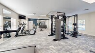 Located at 3325 Oak Forest Dr in Fayetteville, NC, this fitness center offers a comprehensive and thoughtfully organized workout facility spread across a single floor. The space is designed to accommodate a wide range of fitness activities, from cardiovascular training to strength and functional fitness.

The cardio zone features a row of treadmills and spinning bikes positioned along the windowed wall, where natural light filters in through multiple windows fitted with blinds. Wall-mounted televisions provide entertainment during workouts. Large mirrors are strategically placed throughout to enhance the sense of space and allow for form monitoring.

The strength training area is well-appointed with a multi-functional cable and pulley machine system, a dedicated free weight section with a full rack of dumbbells, stability balls, resistance bands, and a weight bench with additional attachments. The functional fitness zone includes an air bike, step platforms, and battle ropes for high-intensity training.

The flooring throughout consists of durable, patterned carpet tiles in a neutral gray tone, complementing the light-colored walls with a navy blue accent wall near the free weight area. Recessed panel lighting ensures the space is well-lit throughout. The open floor plan allows for easy navigation and simultaneous use of multiple equipment stations, making this fitness center a versatile and fully equipped facility.