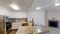 This single-floor, two-bedroom, two-bathroom residence at Azure Falls offers a thoughtfully designed layout with functional and attractive finishes. The kitchen is a standout feature, showcasing granite countertops with warm, neutral toning that extend across a generous breakfast bar — an ideal space for casual dining or entertaining. White cabinetry provides ample storage while contributing to a clean, bright aesthetic, complemented by a stainless steel double-basin sink and modern hardware. Flush-mount ceiling lighting illuminates both the kitchen and the adjacent living area effectively. The flooring features wood-style planking that adds warmth and continuity throughout the open-concept space. The transition between the kitchen and living area is seamless, creating an open, connected feel that maximizes the sense of space. Neutral wall tones throughout provide a versatile backdrop suitable for a variety of décor styles. The textured ceiling detail adds a subtle architectural element to the interior. Overall, the residence presents a well-maintained, move-in-ready environment with practical amenities and a comfortable, welcoming ambiance throughout.