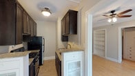 This single-floor residence offers a thoughtfully designed layout that balances classic character with functional living. The galley-style kitchen is a standout feature, lined on both sides with rich dark-stained cabinetry that extends to the ceiling, providing ample storage. Granite countertops run the length of both walls, complemented by a stainless steel sink and black appliances, including a gas range and refrigerator. Distinctive white base cabinets with glass panel doors add a contrasting design detail. The living and bedroom areas are finished with light hardwood flooring and neutral-toned walls, creating a bright and open atmosphere. Crown molding and ceiling fans are present throughout, adding a touch of classic architectural detail. Built-in shelving units provide practical and attractive display or storage space. A generous walk-in closet with rod storage and hardwood flooring offers excellent wardrobe organization. Windows in the living areas invite natural light and outdoor views. The bathroom is finished in clean white tile, featuring a combined tub and shower, a vanity with a mirror medicine cabinet, and a window that provides natural ventilation and light.