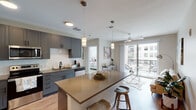 This well-appointed single-floor residence offers a cohesive modern aesthetic throughout its thoughtfully designed layout. The open-concept kitchen serves as the heart of the space, showcasing gray shaker-style cabinetry extending to the ceiling, a white subway tile backsplash, and a full suite of stainless steel appliances, including a refrigerator, range, microwave, and dishwasher. A generously sized island with a warm taupe countertop provides seating and additional workspace, illuminated by stylish pendant lighting. Light wood-style flooring runs throughout the main living areas, enhancing the bright, airy atmosphere. Large sliding glass doors open to a private balcony, bringing in natural light and urban views.

The unit includes two bedrooms, each fitted with plush carpet, ceiling fans, and broad windows that invite natural light. One bedroom benefits from direct access to a walk-in closet. The two bathrooms are finished with white cabinetry featuring matte black hardware, dark countertops, and tile flooring. The primary bath includes an elongated vanity and walk-in closet access, while the secondary bath offers a full tub-shower combination. A dedicated laundry area completes the practical and polished interior.