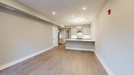 Located at 85 Martin Luther King Ave in Morristown, NJ, this single-floor unit offers a thoughtfully designed layout with modern finishes throughout. Light gray luxury vinyl plank flooring runs continuously across the space, creating a cohesive and clean aesthetic. The open-concept kitchen is a standout feature, boasting white shaker cabinetry, a striking marble-look quartz waterfall island with seating, a subway tile backsplash, stainless steel appliances including a refrigerator and range, and a stainless steel wall-mounted range hood, all illuminated by a contemporary chandelier and recessed lighting. The living area flows naturally from the kitchen, offering generous open space. A dedicated entry area features a classic wood-paneled front door flanked by a window that draws in natural light and outdoor views of the surrounding neighborhood. The bedrooms are calm and well-proportioned, with neutral warm-gray walls and ample natural light from double-pane windows. The bathroom is finished with a white vanity, quartz countertop, large mirror, and tile flooring. Additional highlights include an in-unit laundry area, a built-in desk surface, recessed lighting throughout, and crisp white millwork. The overall ambiance is clean, modern, and move-in ready.