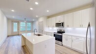 This thoughtfully laid out 2-bedroom, 2-bathroom single-story home at 190 Moll Rd offers a clean, modern aesthetic throughout its generously sized floor plan. The open-concept kitchen serves as the heart of the home, featuring a large central island with an undermount sink, crisp white shaker cabinetry, white subway tile backsplash, quartz countertops, and stainless steel appliances including a range, microwave, and refrigerator. Recessed lighting illuminates the space, which flows naturally into the living area. Light wood-look flooring runs throughout the main living spaces, lending warmth and continuity. The primary bedroom is a spacious retreat with a ceiling fan, natural light from a window, and access to a well-appointed en-suite bathroom featuring large-format tile flooring, a glass-enclosed shower, a long vanity with quartz countertops, brushed nickel hardware, and a backlit mirror. A walk-in closet with built-in wire shelving provides generous storage. The second bedroom also features a ceiling fan, a window with outdoor views, and wood-look flooring. A dedicated laundry area houses a full-size washer and dryer. The living area includes access to an outdoor balcony, bringing in natural light and views of surrounding greenery.