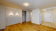 This single-floor unit offers a clean, efficient layout designed to maximize functionality. The main living area is finished with warm, honey-toned hardwood flooring that extends throughout, creating a cohesive and inviting atmosphere. A flush-mount ceiling light and a wall sconce provide layered lighting, while a large window dressed with vertical blinds allows natural light to brighten the space. A built-in closet with sliding doors and open shelving offers convenient storage directly within the living area.

The kitchen is compact yet fully equipped, featuring white cabinetry, a tile backsplash, a white electric range, a refrigerator, and a single-basin sink — all arranged efficiently along one wall. The kitchen transitions to tile flooring, clearly delineating it from the living space.

The bathroom is thoughtfully designed with a generous L-shaped vanity topped with pink-veined marble-style countertops, white cabinetry underneath, and a large mirrored medicine cabinet above the sink. A glass-enclosed shower stall completes the bathroom. Light tile flooring and a well-placed vanity light contribute to a clean, functional aesthetic throughout.