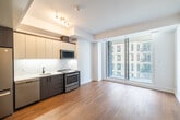 This thoughtfully designed one-bedroom, one-bathroom unit offers a clean, modern aesthetic throughout its efficiently organized single-floor layout. Warm-toned hardwood flooring flows consistently across all living areas, anchoring the bright, contemporary interior.

The open living area is highlighted by large floor-to-ceiling sliding glass doors that invite abundant natural light and offer urban views of the surrounding cityscape. The crisp white walls and clean lines create an airy, minimalist ambiance throughout.

The kitchen is well-appointed with a full suite of stainless steel appliances, including a French-door refrigerator, gas range, built-in microwave, and dishwasher. Two-tone cabinetry — combining dark wood lower cabinets with light upper cabinets — frames a white countertop with a modern undermount sink, all set against a clean white backsplash.

The bedroom is a calm, light-filled retreat, featuring hardwood floors and a generous window with urban views, providing a bright and comfortable space.

The bathroom is a standout feature, finished in elegant marble-effect tile covering both the floor and walls. It includes a walk-in shower with a ceiling-mounted rainfall showerhead, matte black fixtures, a vessel sink atop a white vanity, and contemporary dark wood accents — delivering a spa-like atmosphere with refined, high-end finishes.