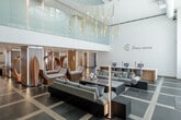 Located at 2277 Harbor Blvd in Costa Mesa, California, this expansive single-floor lobby space at Lux Costa Mesa offers a refined and contemporary environment designed to impress. The space is anchored by a dramatic double-height atrium filled with cascading gold rod chandeliers that draw the eye upward, creating an immediate sense of grandeur upon entry. Floor-to-ceiling sheer curtains flank large glass entry doors, allowing an abundance of natural light to flood the interior while framing views of swaying palms outside.

The living area is thoughtfully zoned into distinct seating arrangements, featuring plush neutral-toned sofas, sculptural lounge chairs, and sleek low-profile coffee tables atop a geometric slate-and-wood tile floor. A striking teal hexagonal mosaic tile fireplace wall serves as a bold focal point in one section of the space, complemented by a live-edge wood coffee table and deep navy velvet seating nearby.

Warm wood paneling, backlit architectural columns, and artistic sculptural installations contribute to the space's coastal-luxury aesthetic. A co-working area with clean white desks and modern workstations provides a functional counterpoint to the lounge zones, while a café-style seating area is defined by an ornate coral-motif room divider. Together, these elements create a cohesive, upscale atmosphere that is both welcoming and architecturally distinctive.