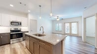 Located at 171 Town Park Dr in Conroe, TX, this thoughtfully designed one-bedroom, one-bathroom residence offers a comfortable and functional single-floor layout. The open-concept living area seamlessly connects the kitchen, dining, and living spaces, all finished with light-toned hardwood-style flooring and neutral walls that maximize brightness throughout.

The kitchen is a standout feature, showcasing a large granite-topped island with a single-basin sink and stylish pendant lighting overhead. Two-tone cabinetry — white upper cabinets paired with gray lower cabinets — frames a hexagonal tile backsplash, while stainless steel appliances, including a refrigerator, range, and over-the-range microwave, complete the space. A pantry adds additional storage convenience. The living room opens directly to a private balcony through French doors, inviting natural light and outdoor access.

The generously sized primary bedroom features plush carpet, a ceiling fan, and multiple windows offering neighborhood views. It is complemented by a spacious walk-in closet with built-in shelving. The bathroom impresses with an L-shaped double vanity topped with granite counters, dual framed mirrors, and warm wood-toned cabinetry. A dedicated laundry area rounds out this well-equipped residence.