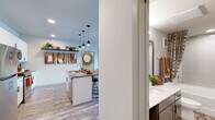 Located at 1561 Brayden Pt in Colorado Springs, CO, this single-story residence offers two bedrooms and two full bathrooms within a thoughtfully designed floor plan. The entrance leads into a kitchen featuring stainless steel appliances, white cabinetry, a peninsula with pendant lighting, and open shelving — flowing seamlessly into the living area. The living room provides access to an outdoor balcony through a glass door, allowing natural light to fill the space. Wood-look plank flooring extends throughout the main living areas, complementing the neutral color palette. The spacious primary bedroom includes a ceiling fan, plush carpet, and a walk-in closet, while the en-suite bathroom offers a double-sink vanity with white quartz countertops and a separate shower. The second bedroom features large windows and soft carpet. The second bathroom includes a soaking tub, tiled surround, and a wide vanity. A stacked washer and dryer unit is conveniently integrated within the unit. Recessed lighting and modern fixtures contribute to a clean, contemporary ambiance throughout.