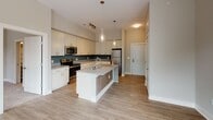 Located at 257 Broadway St. in Asheville, North Carolina, this single-floor unit offers a thoughtfully designed layout with modern finishes throughout. The open-concept kitchen serves as a central hub, featuring white shaker-style cabinetry, granite countertops, a large center island with an undermount sink and pendant lighting, stainless steel appliances, and a teal tile backsplash that adds a pop of color. Light wood-look flooring extends through the kitchen and into the living area, creating a seamless flow. The living space is generously proportioned and bathed in natural light through multiple large windows that frame views of the surrounding Asheville neighborhood. A ceiling fan adds comfort and functionality to the room. The bedroom is a calm, carpeted retreat with its own window providing natural light and outdoor views, also equipped with a ceiling fan. The bathroom is finished with stone-look tile flooring, a granite-topped vanity with white cabinetry, a walk-in shower with white tile surround, and access to a dedicated walk-in closet. Neutral warm-toned walls throughout lend a clean, cohesive aesthetic, making this Asheville unit a well-balanced and move-in ready space.