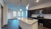 This single-floor unit showcases a contemporary open-concept layout, with the kitchen and living area seamlessly connected. The kitchen is a standout feature, equipped with dark espresso cabinetry extending to the ceiling and a white subway tile backsplash that provides striking contrast. A central island with a granite countertop and undermount sink serves as both a functional workspace and a natural dividing point between the kitchen and living area. Pendant lights hang above the island, complementing the recessed lighting throughout. Stainless steel appliances, including a refrigerator, electric range, and microwave, complete the kitchen's modern aesthetic. Wood-style flooring runs throughout the main living areas, adding warmth and continuity. Multiple windows fitted with horizontal blinds allow natural light to fill the open living space, which also features a ceiling fan. The bathroom includes a tiled tub-shower combination, a dark vanity with granite countertop and undermount sink, and wood-style flooring. The bedroom offers a carpeted floor and a generously sized window that invites natural light into the room, creating a calm and comfortable environment. The overall design maintains a cohesive, modern palette throughout.