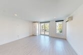 Located at 42 N Beacon St, Unit 203 in Boston's Allston neighborhood, this thoughtfully designed unit offers a clean, modern aesthetic throughout. Light-toned hardwood-style flooring runs continuously across the space, complementing the crisp white walls and recessed lighting that create a bright, airy atmosphere.

The living room is the heart of the unit, featuring sliding glass doors that open to a private balcony, flooding the space with natural light and offering pleasant outdoor views of surrounding greenery. A wall-mounted mini-split system provides efficient climate control. Built-in cabinetry adds functional storage without compromising the open feel of the room.

The kitchen is well-appointed with high-gloss white cabinetry, white quartz countertops, and a classic subway tile backsplash. Stainless steel appliances — including a refrigerator, electric range, over-the-range microwave, and dishwasher — complete this modern culinary space, which flows seamlessly into the main living area.

The bathroom features large-format tile flooring, a subway-tiled tub-shower combination, a warm wood-toned vanity with a white countertop, and a well-lit mirror. The entrance provides a practical transition into the unit with convenient access to the main living and kitchen areas.