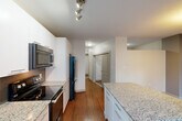 Located on Jasper Avenue NW in the heart of Edmonton, Alberta, this one-bedroom, one-bathroom unit offers a thoughtfully designed layout that maximizes every square foot of its compact footprint. Warm hardwood flooring flows throughout, complementing the neutral tones that give the space a clean, modern aesthetic.

The open-concept living, dining, and kitchen area forms the heart of the unit. The kitchen is a standout feature, showcasing sleek white cabinetry, granite countertops with a generous island overhang, a mosaic tile backsplash, and stainless steel appliances including a built-in microwave, electric range, and a large French-door refrigerator. Track lighting overhead ensures excellent task illumination, while a floor-to-ceiling window bathes the kitchen and living area in natural light and provides views of the surrounding Edmonton cityscape.

The hallway leads to the private bedroom, a cozy retreat featuring sliding double closet doors and a textured ceiling. A second closet provides additional storage. The bathroom is clean and functional, offering a full soaker tub with shower, a tall built-in linen cabinet, and wood-toned flooring. A dedicated laundry area adds in-suite convenience. Two closets throughout the unit ensure ample storage for everyday living.