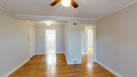 This single-floor, 2-bedroom, 1-bathroom home delivers a comfortable and functional layout across a well-proportioned footprint. Warm hardwood flooring flows consistently throughout the living areas and bedrooms, lending a sense of continuity and character to the space. Crown molding and ceiling fans are present throughout, adding classic detail and practical comfort.

The main living area is bright and open, with multiple doorways connecting to the rest of the home. A central hallway provides efficient access to all rooms. Both bedrooms are generously sized, each featuring hardwood floors, ceiling fans with light fixtures, crown molding, and multiple windows that invite abundant natural light and views of the surrounding greenery. The dual-window configurations in each bedroom create an airy, well-lit atmosphere.

The kitchen is bright and efficient, featuring white cabinetry, ample counter space, a stainless steel sink, and a pair of windows that fill the room with natural light. The full bathroom is clean and straightforward, finished in white tile with a full-size tub and shower combination, a toilet, and a window for natural ventilation. The overall aesthetic throughout the home is clean and neutral, with light gray walls providing a versatile backdrop ready for personalization.
