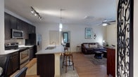 This single-story residence offers a thoughtfully designed open-concept layout that seamlessly connects the kitchen, dining, and living areas. The kitchen is outfitted with dark espresso cabinetry, granite countertops, a tile backsplash, stainless steel appliances including a French door refrigerator and built-in microwave, and a peninsula with bar seating. Pendant and track lighting illuminate the space, while wood-style flooring flows throughout the main living areas.

Adjacent to the kitchen, a dedicated dining nook accommodates a round glass-top table and seating for four, accented by framed wall art. The living room features a ceiling fan, natural light from a large window with outdoor views, and wood-style flooring underfoot.

Two bedrooms offer plush carpeting, ceiling fans, and generous natural light through large windows. One bedroom includes a spacious walk-in closet fitted with wire shelving. The bathroom features a soaking tub with tile surround. A dedicated laundry area houses a full-size washer and dryer, adding everyday convenience to this well-rounded residence.