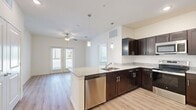 This 2-bedroom, 2-bathroom residence offers a thoughtfully designed single-floor layout that maximizes comfort and functionality. The open-concept kitchen serves as the heart of the home, showcasing rich dark espresso cabinetry, granite countertops, a peninsula with pendant lighting, and a full suite of stainless steel appliances including a refrigerator, range, microwave, and dishwasher. Light wood-style flooring flows throughout the main living areas, complementing the neutral wall tones and creating a bright, cohesive atmosphere. The living area benefits from natural light through multiple windows and a glass door, enhanced by a ceiling fan overhead. Both bedrooms are carpeted for warmth and comfort, with the primary bedroom offering a generous walk-in closet equipped with wire shelving. Each bathroom features dark cabinetry with granite countertops, a single vanity sink, and wood-style flooring, maintaining a consistent design aesthetic throughout. The secondary bathroom includes overhead lighting and additional cabinet storage. A hallway with two closets provides ample storage. The clean, modern finishes and efficient floor plan make this a practical and attractive living space.