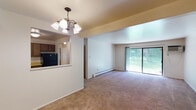 Located at 2131 Tanglewood Pl in Hammond, Indiana, this single-floor residence offers a practical and comfortable layout with well-defined living spaces throughout. The open living and dining area is finished with neutral carpet and features a chandelier overhead, baseboard heating, and a pass-through opening that connects seamlessly to the kitchen, creating an airy, connected feel. Large sliding glass doors flood the living room with natural light and provide direct views of the lush green outdoors. The kitchen is well-appointed with dark wood cabinetry, ample counter space, a double-basin sink, and black appliances including a gas range and refrigerator, all set on easy-care vinyl flooring. The bedrooms are carpeted and bright, with windows that bring in natural light and views of the surrounding greenery, complemented by baseboard heating for year-round comfort. The home includes two bathrooms: one featuring a walk-in shower with a chrome-framed glass enclosure and tile flooring, and another with a full soaking tub and shower combination, a vanity with storage, and a mirror. A wall-mounted air conditioning unit provides additional climate control in the living area. Overall, the space presents a functional and inviting layout suited for comfortable everyday living.