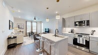 Located in Frisco, TX, this well-appointed 2-bedroom, 2-bathroom unit offers a thoughtfully designed single-floor layout. The open-concept kitchen and living area serves as the heart of the home, featuring gray shaker-style cabinetry with gold hardware, white quartz countertops, stainless steel appliances, and a central island with seating — illuminated by elegant pendant lighting. Wood-look flooring flows seamlessly throughout the space, adding warmth and continuity. The living room is bright and welcoming, with multiple windows allowing generous natural light and a ceiling fan overhead. Each bedroom is comfortably sized, with the primary bedroom offering dual windows with outdoor views and dedicated closet space. The second bedroom mirrors this comfortable feel with its own closet. Both bathrooms are finished with crisp white marble-style tile surrounds in the tub-shower combinations, matte black fixtures, and distinctive patterned floor tile that adds a striking design detail. A hallway connects the rooms efficiently, completing this clean, modern layout that balances style and function throughout.