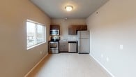 This single-floor unit offers a well-organized and functional layout designed to maximize every square foot. The kitchen is a standout feature, outfitted with a full suite of stainless steel appliances including an electric range, over-the-range microwave, dishwasher, and refrigerator. Rich, dark-toned cabinetry provides ample storage above and below, while granite-style countertops add a polished finish. A single-basin sink is positioned conveniently at the center of the counter. Light-toned luxury vinyl plank flooring runs throughout the space, lending a clean and cohesive look to each room. The main living area is open and bright, benefiting from natural light through a large window. The bedroom is a comfortable, well-proportioned room featuring its own window for additional natural light and a wall-mounted HVAC unit for climate control. The bathroom is neatly appointed with a walk-in shower stall, a toilet, and a vanity topped with granite-style countertop and dark cabinetry consistent with the kitchen's design. Chrome fixtures and a towel bar complete the bathroom's practical finishes. Neutral wall tones throughout the space create a calm and adaptable environment suitable for a variety of furnishing styles.