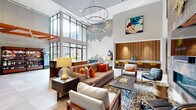 Located at 465 Memorial Dr SE in Atlanta's Grant Park neighborhood, this well-appointed amenity space delivers a thoughtfully designed, multi-functional environment across a single open floor plan. Soaring double-height ceilings with dramatic orange structural beams create an immediate sense of volume and architectural character upon entry, where floor-to-ceiling glass doors flood the space with natural light and offer views of a landscaped courtyard and pool area beyond.

The main lounge is anchored by a striking floor-to-ceiling textured stone accent wall that serves as a bold focal point, complemented by a circular chandelier with cascading Edison-style bulbs, curated contemporary artwork, and a built-in bar counter with stylish seating. Large-format stone tile flooring runs throughout, lending a clean, modern aesthetic.

A private conference or gathering room is accessed through oversized sliding barn doors crafted from reclaimed wood with geometric glass insets, revealing an intimate interior with patterned tile flooring, pendant lighting, a conference table, and leather seating — ideal for meetings or private events.

A self-serve market area rounds out the space, featuring well-stocked retail shelving, a beverage station, and a self-checkout kiosk, providing everyday convenience. A decorative hexagonal tile feature wall and additional seating areas complete this vibrant and functional communal hub.