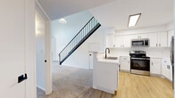 This two-story home in Bloomington, MN offers a well-designed layout spread across two floors. The main level features an open-concept kitchen and living area, where light hardwood flooring runs throughout the kitchen and transitions to plush carpet in the living space. The kitchen is outfitted with crisp white shaker cabinets, black hardware accents, stainless steel appliances including a refrigerator, range, and over-the-range microwave, and a peninsula with a sink. A striking black metal staircase railing serves as a focal point, adding a modern contrast to the bright, white walls throughout. Natural light fills the living area, which includes a sliding glass door leading to a private balcony with views of surrounding trees. The upper level hosts two bedrooms, including a spacious primary bedroom with a walk-in closet featuring built-in wire shelving. Bedrooms are carpeted and receive ample natural light through large windows. Two full bathrooms, each with a tub-shower combination and hardwood-style flooring, serve the home. A versatile loft area on the upper level provides additional flexible living space. Hallways and closets on both floors add to the home's practical storage and circulation.