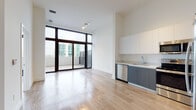 Located at 1120 SW 31st Ave in Miami's vibrant 33135 corridor, this contemporary single-floor residence showcases a clean, modern design with an open-concept living and kitchen area bathed in natural light. Expansive floor-to-ceiling glass walls and sliding doors frame sweeping urban views of the Miami skyline, seamlessly connecting the interior to a private outdoor balcony — ideal for enjoying South Florida's year-round climate.

The kitchen is well-appointed with two-tone cabinetry featuring white upper cabinets and slate-gray lower units, complemented by stainless steel appliances including a side-by-side refrigerator, electric range, built-in microwave, and dishwasher. Light wood-toned flooring flows continuously throughout the living spaces, enhancing the bright, airy atmosphere created by the generous ceiling height.

The bedroom enjoys the same impressive floor-to-ceiling glazing and direct balcony access, offering an abundance of natural light and open city views. The bathroom is finished with large-format stone-effect floor tiles and striking wood-look wall tiles surrounding the soaking tub and shower, paired with a sleek floating vanity in a dark finish. This residence delivers a polished, contemporary living experience in the heart of Miami.