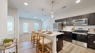 Located at 3111 Hayden Rd in Columbus, Ohio, this one-bedroom, one-bathroom residence offers a thoughtfully designed single-floor layout that maximizes both functionality and style. The open-concept living area seamlessly connects the kitchen, dining, and living spaces, creating an inviting, cohesive environment bathed in natural light from multiple windows.

The kitchen is a standout feature, showcasing dark espresso cabinetry paired with crisp white quartz countertops and a full suite of stainless steel appliances. A central island with a built-in sink and bar seating — illuminated by two globe pendant lights with gold-toned hardware — serves as an ideal casual dining and entertaining hub. Light wood-tone luxury vinyl plank flooring runs throughout the main living areas, adding warmth and a modern aesthetic.

The bedroom is a comfortable retreat, featuring plush carpeting, a generously sized window with outdoor views, and access to two closets for ample storage. The bathroom continues the refined design language with dark cabinetry, a white vanity top, and wood-look flooring. A dedicated laundry area and a private balcony round out the unit's practical offerings, providing both convenience and outdoor access.