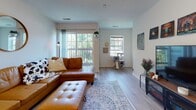This single-floor residence offers a practical and comfortable layout designed for everyday living. The entryway welcomes you with light wood-style flooring that flows into the main living spaces, providing a warm and cohesive foundation throughout.

The living room is a bright, inviting space featuring large sliding glass doors that open to a private balcony, filling the room with natural light and offering views of surrounding greenery. A second window further enhances the airy atmosphere.

The kitchen is thoughtfully equipped with white cabinetry, ample counter space, and a full suite of appliances including a range, dishwasher, and built-in microwave. Tile flooring and a skylight-style overhead fixture complete the functional design.

The primary bedroom is generously sized with plush carpeting, a window overlooking the outdoors, and direct access to an en-suite bathroom. The bathroom features a vanity with warm-toned countertops, tile flooring, and a shower/tub combination. A walk-in closet and additional mirrored closet provide excellent storage.

A secondary bedroom or flex room offers carpeted flooring, a window with natural light, and ample space for use as a home office or guest room. An additional full bathroom serves this area of the home, maintaining the same consistent, clean finishes found throughout the residence.