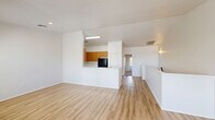Located at 647 West Baseline Road in Tempe, Arizona, this two-story home offers three bedrooms and three bathrooms across a thoughtfully laid-out floor plan. The main level serves as the social hub of the home, featuring an open-concept kitchen and living room that flow seamlessly together. The kitchen is equipped with warm honey-toned wood cabinetry, a white countertop peninsula with an integrated sink, and a full suite of black appliances. Light wood-style flooring runs throughout the main level, enhancing the bright, airy feel. The living area receives generous natural light through multiple windows fitted with blinds, and a ceiling fan adds comfort to the space. A carpeted staircase with a sleek metal railing leads to the upper level, where the bedrooms are situated. The generously sized primary bedroom features plush carpet and a ceiling fan, while a walk-in closet with built-in shelving and hanging rods provides ample storage. Additional bedrooms also feature soft carpet flooring. The bathrooms are clean and functional, each featuring a wood-toned vanity with white countertops, a tub-shower combination, and a large mirror. The home's neutral white walls and consistent finishes throughout create a cohesive, move-in-ready aesthetic.