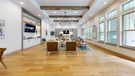 Located at 401 Nonaville Rd in Mount Juliet, Tennessee, this single-story community clubhouse showcases a thoughtfully designed modern farmhouse aesthetic that seamlessly blends warmth and contemporary style. The open-plan interior is anchored by wide-plank light hardwood flooring that flows continuously throughout, creating a cohesive and inviting atmosphere.

Exposed wood ceiling beams contrast beautifully against white shiplap walls and a painted tongue-and-groove ceiling, lending the space a refined yet relaxed character. Recessed lighting, complemented by statement pendant and chandelier fixtures, ensures the space is well-lit at all hours. A generous bank of large, multi-pane windows lines one wall, flooding the interior with natural light and offering views of the surrounding landscape.

The main gathering area is organized into distinct yet open seating zones, featuring a curated mix of lounge chairs, sofas, and ottomans arranged around area rugs — ideal for both casual socializing and quiet relaxation. A built-in media console with white cabinetry, dark countertops, and a wall-mounted display screen serves as a functional focal point along one wall, framed by warm wood shelving detail.

Toward the rear, sage-green cabinetry and a stylish backsplash define a kitchenette or refreshment area, while a long communal dining table with pendant lighting provides a dedicated space for gatherings or collaborative use. The overall ambiance is warm, polished, and welcoming.