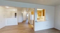 This upgraded single-floor residence offers a spacious and thoughtfully designed layout across a generous footprint. The open floor plan allows for a natural flow between living areas, enhanced by light-toned luxury vinyl plank flooring that runs throughout, lending warmth and a clean, contemporary feel.

The kitchen is positioned to one side and features a pass-through counter that connects it to the main living area, promoting an open and accessible atmosphere. Honey-toned wood cabinetry provides ample storage, and white appliances — including a full-size refrigerator — offer functional, everyday convenience. Under-cabinet lighting adds a practical touch to the workspace.

A wide central hallway connects the main living space to the bedroom, which includes a spacious closet with built-in shelving and hanging storage — ideal for maximizing organization. The overall color palette throughout the unit is neutral and bright, with white walls that allow natural light to move freely through the space. Additional doors along the hallway provide access to further storage and the bathroom. The result is a well-balanced, move-in-ready home that combines practicality with upgraded finishes.