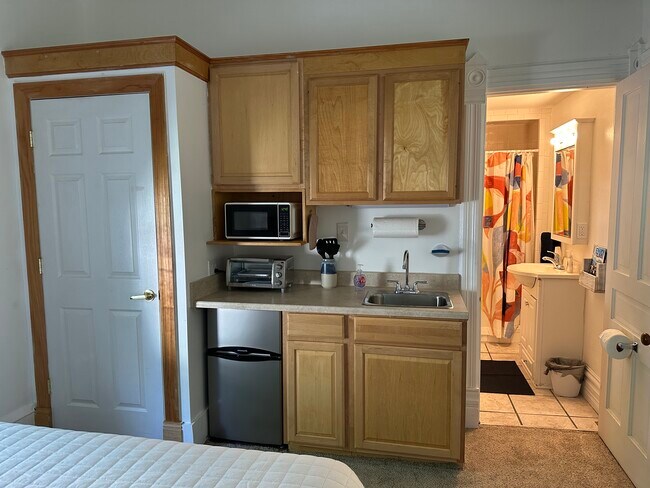 Cocina pequeña con nevera pequeña, tostadora, microondas y hornilla eléctrica. Armario a la izquierda, baño a la derecha. - 305 S Elm St