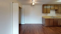 This single-floor, one-bedroom, one-bathroom unit delivers a practical and comfortable layout designed for efficient everyday living. The living area features rich hardwood-style flooring, a ceiling fan with integrated lighting, and a textured ceiling. A sliding closet and an adjacent door provide convenient storage and passage, while the space flows naturally into the kitchen area.

The galley-style kitchen is well-appointed with warm wood cabinetry spanning both walls, offering generous upper and lower storage. Light-toned countertops run the length of the kitchen, accompanied by a double stainless steel sink, an electric range with coil burners, a full-size refrigerator, and a dishwasher — all essential appliances in place.

The bedroom is a comfortable, carpeted retreat with a window that brings in natural light and views of greenery outside. A textured ceiling and neutral walls keep the room bright and versatile.

A secondary carpeted space, also with a ceiling fan, connects the living area to the rest of the unit, offering additional flexibility. The bathroom features wood-style vinyl flooring, a full tub-shower combination, a wood-toned vanity with a single sink, and clean, light-colored walls that contribute to a crisp, tidy feel throughout.
