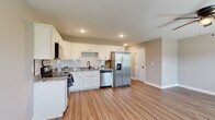 This two-story home is designed with a clean, contemporary aesthetic and consistent finishes throughout. The kitchen serves as a functional centerpiece, featuring white shaker-style cabinetry, granite countertops, a classic subway tile backsplash, and a full suite of stainless steel appliances including a range, dishwasher, over-the-range microwave, and a side-by-side refrigerator with an in-door water and ice dispenser. Light wood-look flooring runs through the kitchen and connecting areas, lending warmth and cohesion to the main living spaces.

A well-lit hallway connects the upper level, where multiple bedrooms are finished with plush carpeting, neutral gray walls, and ceiling fans fitted with lighting. Each bedroom benefits from natural light through windows with white blinds, creating bright and comfortable spaces. The primary bedroom includes multiple doors leading to additional spaces, suggesting a walk-in closet and en suite access.

The bathrooms are consistently appointed with white vanity cabinetry, granite countertops, wood-look flooring, and tub-shower combinations. The overall palette of soft grays, crisp white trim, and warm wood tones gives the home a modern yet welcoming character throughout both floors.