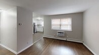 This single-floor unit at 203 S Macdade Blvd in Glenolden, PA offers a well-organized layout with a consistent, clean aesthetic throughout. Rich, dark hardwood flooring runs through the living areas and bedrooms, providing a warm contrast to the neutral gray and white walls found in every room.

The living area is open and functional, with a window allowing natural light to filter in and a wall-mounted air conditioning unit for climate control. Baseboard heating is present throughout the unit. The space flows directly into the kitchen, which features white shaker-style cabinetry, granite-look countertops, a stainless steel refrigerator, dishwasher, electric range, and over-the-range microwave. A window above the sink adds natural light to the cooking area.

Two well-proportioned bedrooms each include a window with exterior views and baseboard heating, maintaining the unit's consistent hardwood flooring and neutral palette.

The bathroom is finished in white, with subway tile wainscoting, a toilet, vanity with sink, overhead cabinetry for storage, and baseboard heating. The 3D floorplan reveals a compact but efficiently arranged layout with clear separation between living, sleeping, and utility spaces.