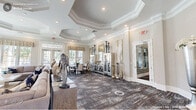 This single-story clubhouse in Durham, NC, offers a generously sized, thoughtfully designed communal space that blends sophistication with comfort. The entrance foyer makes an immediate impression with polished marble-style tile flooring, a tiered crystal chandelier, and a tray ceiling framed by refined crown molding. Large glass-paneled doors flood the space with natural light and provide views of the surrounding community.

The main lounge area features an octagonal tray ceiling, a white marble fireplace flanked by large windows with decorative valances, and plush seating arranged around curated sculptural décor. Patterned carpeting adds warmth and texture throughout this central gathering area.

The kitchen is well-appointed with rich walnut-toned cabinetry, white quartz countertops, a gleaming marble-style tile floor, and a central island with bar seating—ideal for events and casual gatherings. An adjacent dining area provides multiple seating options, including high-top bistro tables and a formal dining set, all bathed in natural light from oversized windows overlooking the community exterior.

Throughout, the clubhouse maintains a cohesive, upscale aesthetic defined by neutral tones, elegant architectural details, and carefully selected décor.