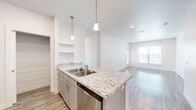This single-story, 3-bedroom, 3-bathroom home in Sapulpa, Oklahoma offers a clean, modern aesthetic throughout. The open-concept kitchen is a standout feature, boasting granite countertops, grey cabinetry with brushed nickel hardware, stainless steel appliances including a refrigerator, range, microwave, and dishwasher, and elegant pendant lighting over the peninsula. Light wood-look flooring runs through the main living areas, complementing the bright, white walls and creating a cohesive, contemporary feel. The living room is bathed in natural light from large windows and offers direct access to an entry door. Each bedroom features plush carpet flooring, a ceiling fan, and closet access, with the primary bedroom offering generous proportions and its own private bathroom complete with a walk-in glass-door shower, granite vanity, and grey cabinetry. Additional bathrooms include a tub-shower combination with brushed nickel fixtures and wood-look tile flooring. A dedicated laundry area houses a full-size washer and dryer with overhead shelving. Two hallways connect the layout efficiently, while a separate closet provides additional storage. The overall ambiance is bright, clean, and move-in ready.