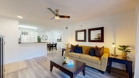 This single-floor residence offers a thoughtfully designed layout that balances comfort and functionality. The living area features durable wood-look flooring, a ceiling fan with light fixture, and a sliding glass door that fills the space with natural light while providing access to an outdoor patio. Framed mirrors and tasteful wall art contribute to the room's clean, contemporary aesthetic.

The kitchen is outfitted with crisp white cabinetry, dark granite-style countertops, tile flooring, and a full suite of white appliances including a range, microwave, dishwasher, and refrigerator. Track lighting overhead ensures excellent task illumination. The adjacent dining area accommodates a full-sized table and chairs, accented by a round mirror and art wall, creating a defined yet open dining space.

The bedroom is a comfortable retreat, featuring wood-look flooring, a ceiling fan, and a large window that brings in generous natural light with views to the outdoors. Two bathrooms serve the residence — one with a tub-shower combination and white tile surround, and a primary bath with an extended vanity, granite-style countertop, a wide mirror with Hollywood-style lighting, and a glass-enclosed shower. The overall design is bright, clean, and move-in ready.