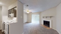 Located at 11500 Huebner Rd in San Antonio, Texas, this single-floor residence offers a well-organized layout with comfortable living spaces throughout. The living room serves as the heart of the home, highlighted by a classic wood-burning fireplace with a tile hearth and a white mantel shelf, plush carpet flooring, and a ceiling fan with integrated lighting. Large sliding glass doors dressed with vertical blinds open to an outdoor patio, filling the space with natural light and providing easy access to the exterior.

The kitchen is conveniently positioned adjacent to the living area, featuring dark cabinetry and a pass-through that connects it to the main living space for an open, functional feel. Multiple bedrooms are carpeted and equipped with ceiling fans. One bedroom includes a walk-in closet with built-in shelving and a window with natural light. Additional bedrooms offer ample space with textured ceilings consistent throughout the home.

The bathroom is outfitted with wood-look vinyl flooring, a dark vanity with a speckled countertop and single-basin sink, a large mirror, and a full-sized tub and shower combo with clean white tile surround. The overall ambiance is neutral and move-in ready, with a consistent palette of soft grays and whites lending a calm, functional character to the entire residence.