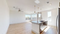 Located at 3939 W 12th St in Houston, TX, this contemporary 2-bedroom, 2-bathroom residence offers a thoughtfully designed single-floor layout with modern finishes throughout. The open-concept kitchen and living area serves as the heart of the home, anchored by a large center island with a quartz countertop, undermount sink, and seating. The kitchen features warm wood cabinetry, a white subway tile backsplash, stainless steel appliances, and globe pendant lights with brass accents that add a refined touch. Light hardwood flooring flows throughout the main living areas, while floor-to-ceiling windows bathe the space in natural light and offer outdoor views. A ceiling fan in the living area enhances comfort. The primary bedroom is generously sized, featuring large windows with sweeping views, and connects to an en-suite bathroom with a dual-sink vanity, rich wood cabinetry, a backlit mirror, and tile flooring. The second bedroom is carpeted, bright, and equipped with a ceiling fan. Both bedrooms include dedicated closets. A clean, well-lit hallway with recessed lighting connects the rooms, completing this polished and functional Houston residence.